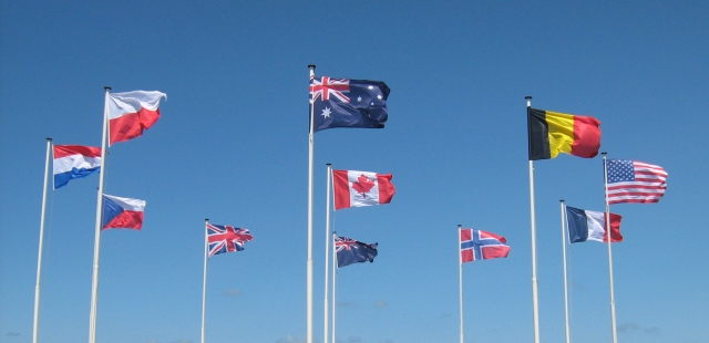 a circle of national flags on poles flying against a blue sky